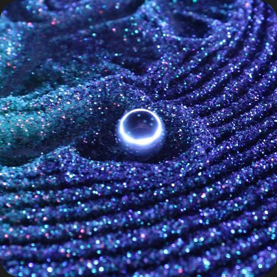 A closeup of a small metal ball carving mesmerizing patterns in glittering blue sand